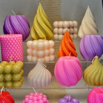 Erimuotoisia ja värisiä kynttilöitä esillä hyllyllä.